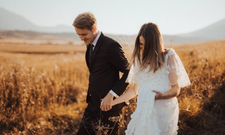 shallow focus photo of man in black formal suit holding woman s hand in white dress