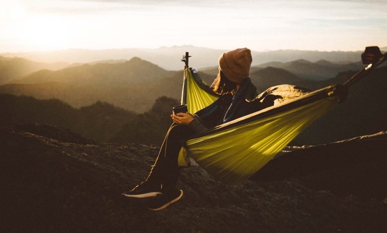 unrecognizable woman sitting in hammock above mountains